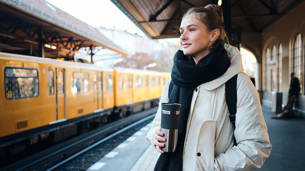 Zniżki PKP dla nauczycieli Młoda kobieta czekająca na peronie z kawą