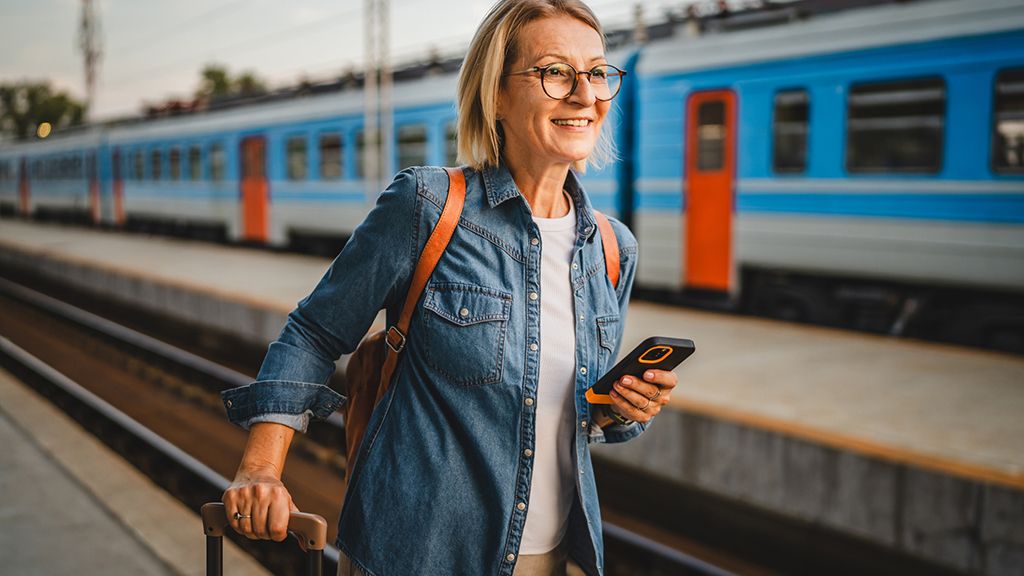 Zniżki PKP dla nauczycieli Kobieta czekająca na peronie z telefonem - Zniżki PKP dla nauczycieli