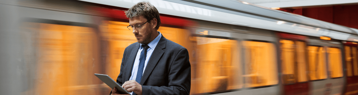 podróże służbowe z PKP mężczyzna z tabletem w ręku na tle pociągu