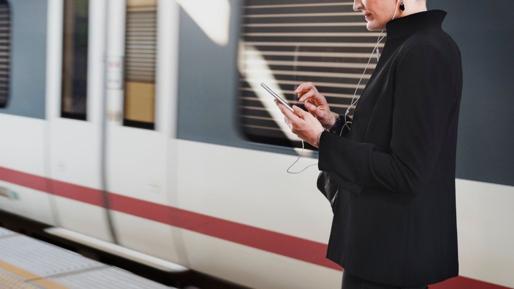 Tablica odjazdów i kasa biletowa Kobieta stojąca na peronie i spoglądająca w telefon komórkowy
